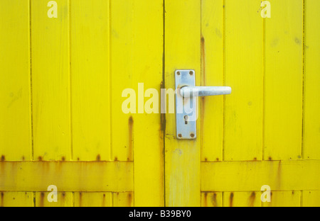 Close up detail of yellow stained wooden door on hut or shed or kiosk or booth with aluminium door handle with rust stains Stock Photo