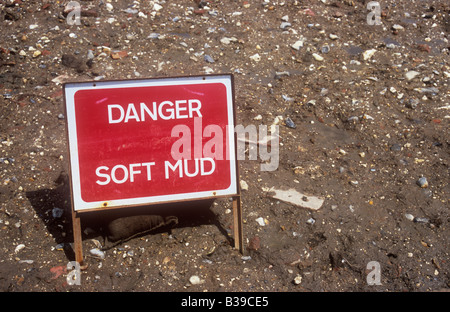 Red and white roadworks sign set in bank of earth with rubble mixed in stating Danger Soft mud Stock Photo
