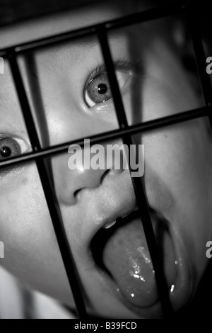 Dramatic baby behind a baby gate portrait with deep shadows Stock Photo