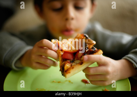 Homemade Pizza Six year old boy tucks into a slice of his mother s home cooking Mixed race Indian ethnic Stock Photo