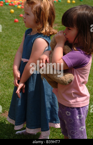 Two girls standing outside, one cuddling a teddy bear and sucking her thumb Stock Photo
