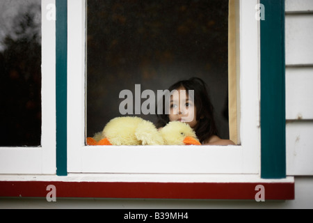 Girl aged 5 looks out window holding soft toy duck Stock Photo