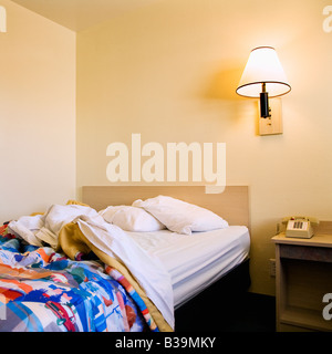Interior shot of motel room with unmade bed and wall lamp Stock Photo