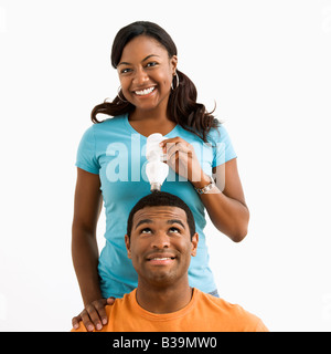 African American female holding energy saving lightbulb over man s head Stock Photo