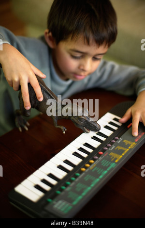T rex plays notes Six year old boy uses toy Tyrannosaurus rex to play notes on electric piano Stock Photo