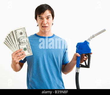 Asian young man with confused expression holding money and gas pump nozzle Stock Photo