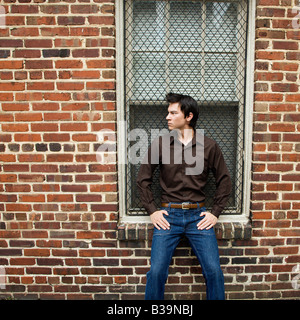 Asian man standing and leaning against window and brick wall Stock Photo