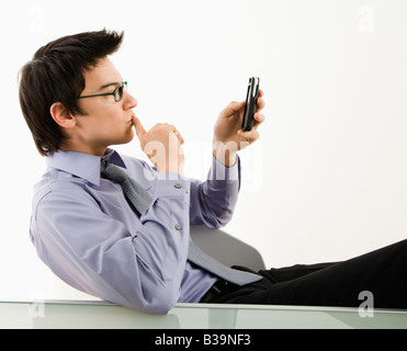 Asian businessman sitting at desk texting using his pda cellphone Stock Photo