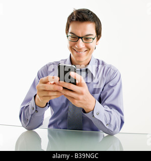 Smiling Asian businessman sitting at desk texting using his pda cellphone Stock Photo