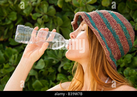 Side view of young redheaded woman wearing hat and drinking from water bottle Stock Photo