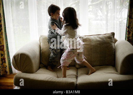 Brother aged six and sister five wrestle on sofa beside window Stock Photo