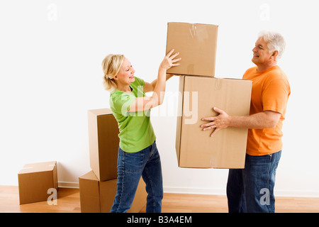 Middle aged man holding cardboard moving boxes while woman places one on stack Stock Photo