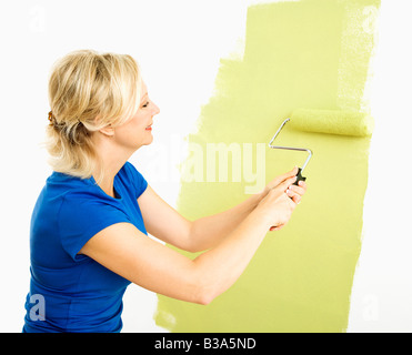 Middle aged woman painting wall green with paint roller Stock Photo