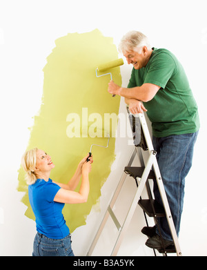 Middle aged couple painting wall green with male on ladder Stock Photo