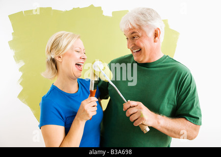 Middle aged couple painting wall green playing with paint utensils Stock Photo