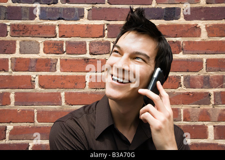 Smiling young Asian man next to brick wall talking on cell phone Stock Photo