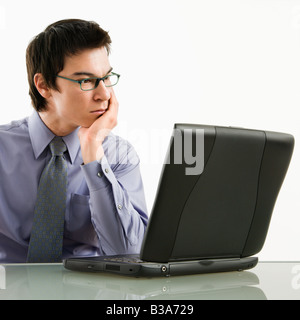 Asian businessman sitting at desk working on laptop computer Stock Photo