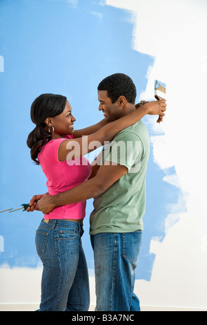 African American couple standing together hugging in front of half painted wall Stock Photo