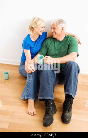 Middle aged couple sitting on floor snuggling and drinking coffee Stock Photo