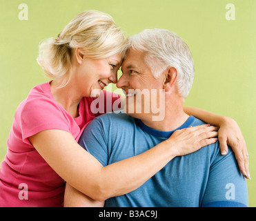 Portrait of smiling middle aged couple in front of green wall snuggling Stock Photo