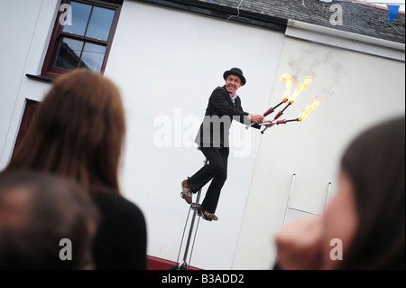 A street performer entertainer riding a unicycle and juggling with fire sticks in Lostwithiel, Cornwall, UK Stock Photo