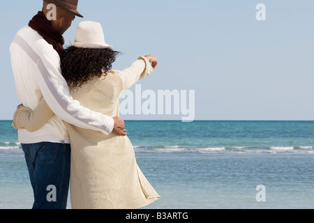 Multi-ethnic couple hugging and pointing at beach Stock Photo