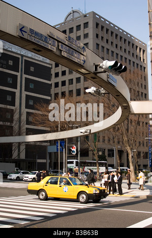 A circular street sign gives directions in the Shinjuku District of Tokyo. A taxi drives over the zebra crossing. Stock Photo