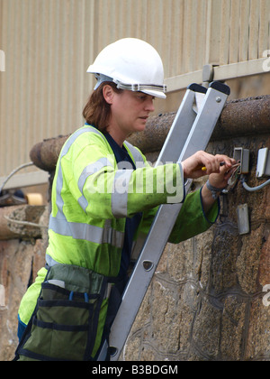 Female electrician wearing a florescent jacket and hard hat, at work. Stock Photo
