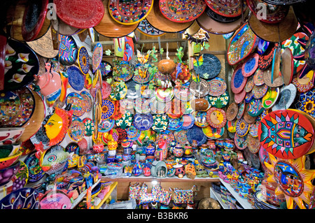 Zihuatanejo Mexico Craft Market Talavera Pottery | ZIHUATANEJO, Mexico — Hundreds of hand-painted ceramic plates, platters, and decorative figures crowd a craft stall in downtown Zihuatanejo. The vivid Talavera-style pottery on display, marked by bold floral, animal, and sun motifs on a white ground, descends from a tradition of Spanish and Moorish tin-glaze tile-making introduced to Puebla in the sixteenth century. Stock Photo