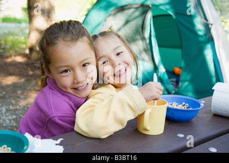 Asian sisters eating at campsite Stock Photo