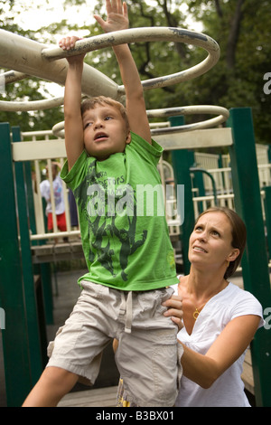 Four year old child building strength and confidence on the monkey bars with his mother nearby Stock Photo
