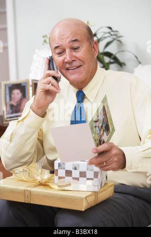 Senior Hispanic man with gifts talking on cell phone Stock Photo