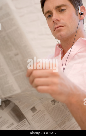 A man listening to headphones reading a newspaper Stock Photo