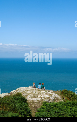 UK, Wales, Pembrokeshire. Three boys sit looking out over Fishguard Bay and the Irish Sea from the Pembrokeshire Coastal Path on Dinas Head. Stock Photo