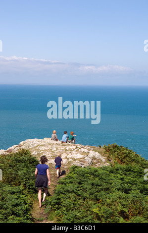 UK, Wales, Pembrokeshire. Three boys sit looking out over Fishguard Bay and the Irish Sea from the Pembrokeshire Coastal Path on Dinas Head. Stock Photo