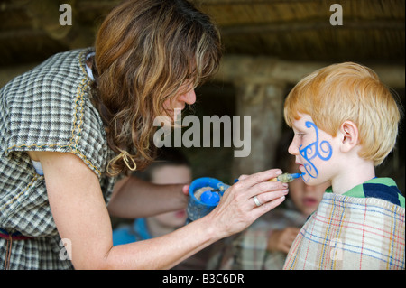 UK, Wales, Pembrokeshire. A young boy has his face painted with woad inn a Celtic symbol by one of the guides at Castle Henllys, a recreated Iron Age Fort built on its original foundations near Newport. Stock Photo