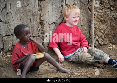 Kenya, Masai Mara National Reserve. During a visit to a Maasai manyatta, a young boy on a family safari poses for a photograph a Maasai child. Stock Photo