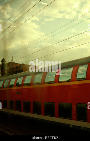 Red German moving train under cloudy sky reflections in windows overhead cables Stock Photo