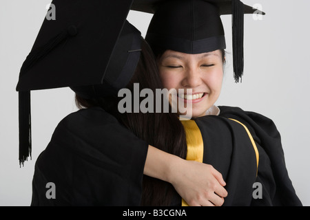 Two female graduates hugging each other and smiling Stock Photo