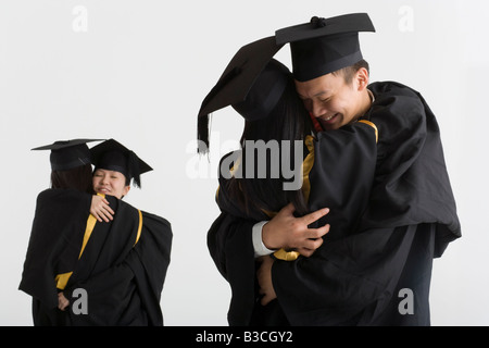 Young male graduate hugging a female graduate and two female graduates hugging in the background Stock Photo