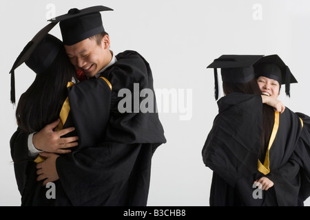 Young male graduate hugging a female graduate and two female graduates hugging in the background Stock Photo