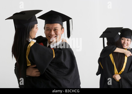 Young male graduate hugging a female graduate and two female graduates hugging in the background