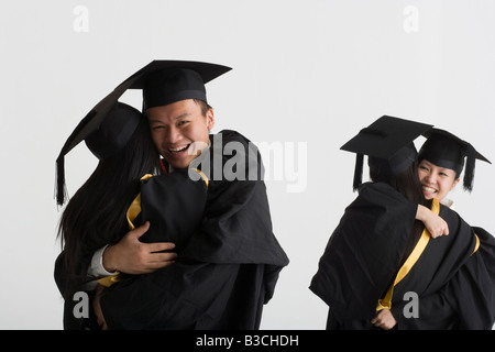Young male graduate hugging a female graduate and two female graduates hugging in the background Stock Photo
