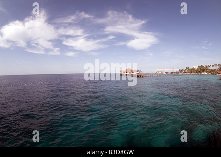 Jetty extending from the beach of Derawan tropical island over crystal clear water below which the coral reef is visible Stock Photo