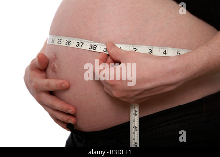 close up 8 month pregnant mid twenties woman 25 years of age measuring baby bump with tape measure showing inches Stock Photo
