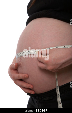 close up of 8 month pregnant mid twenties woman 25 years of age measuring baby bump with tape measure showing inches and metri Stock Photo