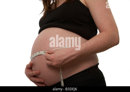 8 month pregnant mid twenties woman 25 years of age measuring baby bump with tape measure showing inches and metric measurements Stock Photo