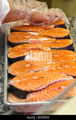 Vendor wearing gloves prepares a tray of farmed Atlantic salmon steaks for sale Stock Photo