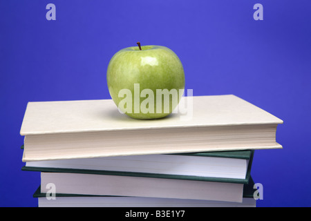 A green apple on a pile of books with a blue background Stock Photo