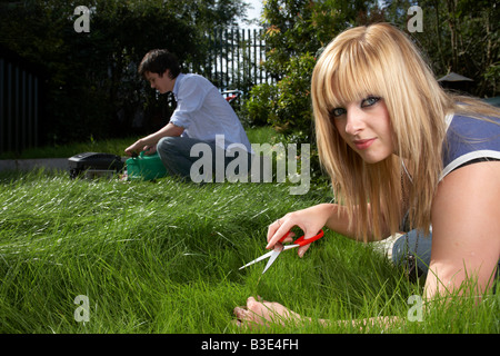 young man woman blonde haired woman dark haired man couple late teens early twenties cutting grass in a garden with scissors Stock Photo
